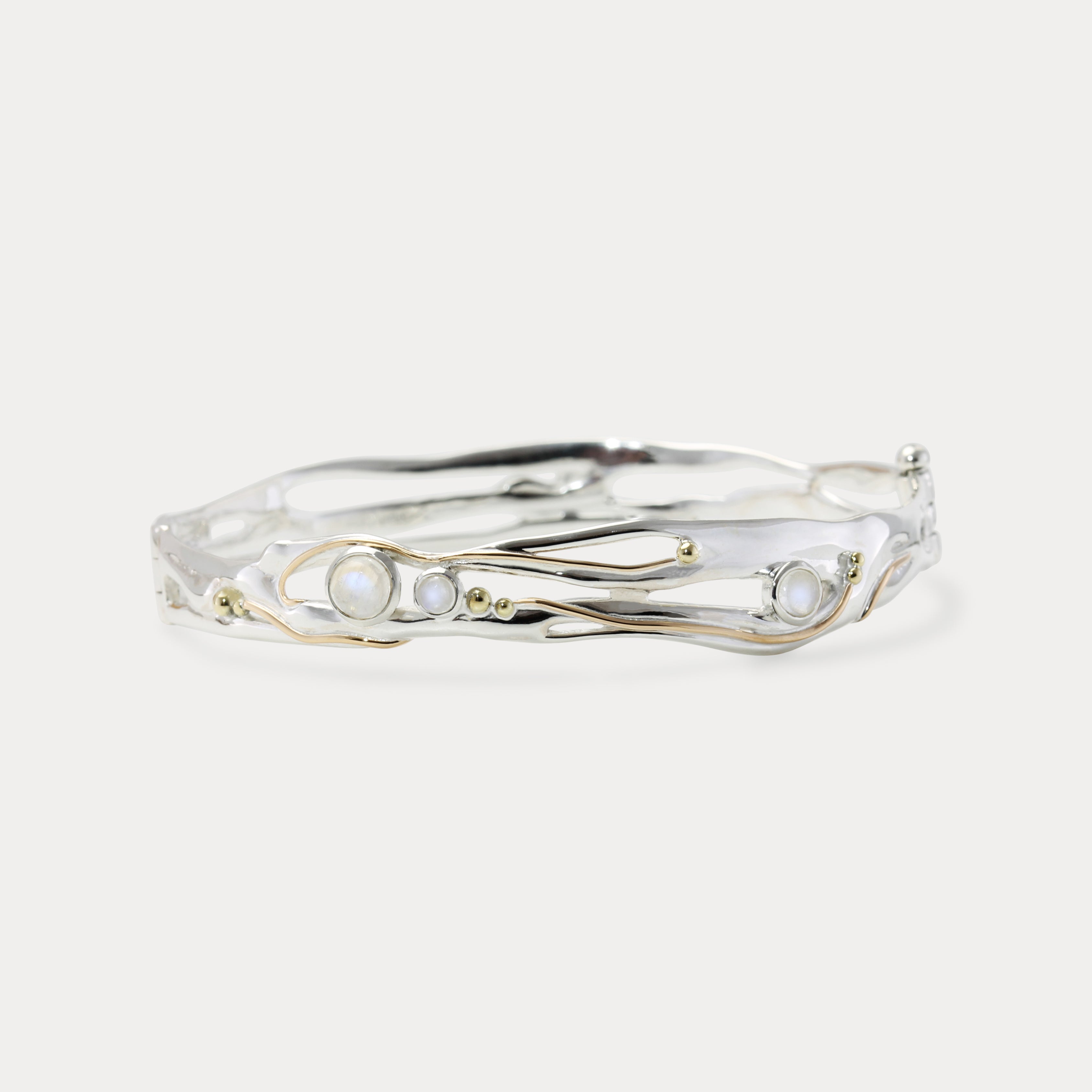 A handmade sterling silver bangle bracelet with moonstone and 14KT gold details, displayed against a white background.