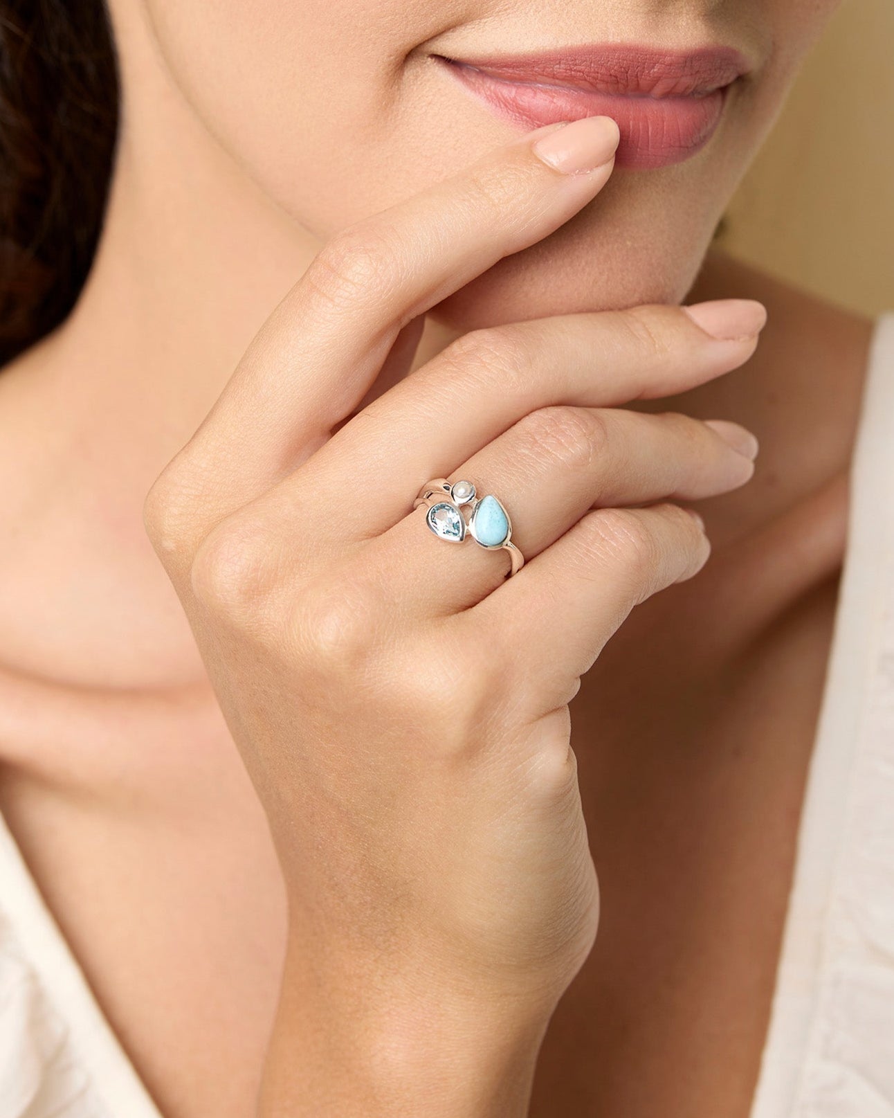 Woman wearing a ring with a blue gemstones, posing thoughtfully with hand on chin.