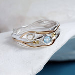 Silver and gold ring with a blue gemstone and white gemstone on a white background