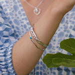 Close-up of a person's arm wearing a silver bracelet with a blue stone, against a blue patterned fabric background.