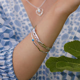 Close-up of a person's arm wearing a silver bracelet with a blue stone, against a blue patterned fabric background.