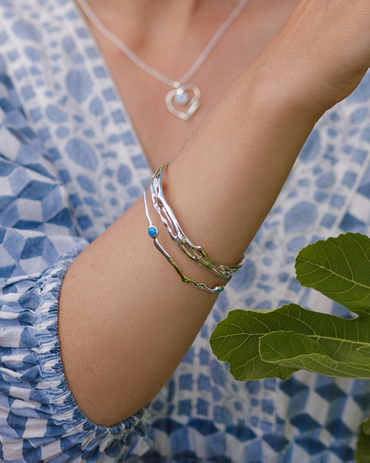 Close-up of a person's arm wearing a silver bracelet with a blue stone, against a blue patterned fabric background.