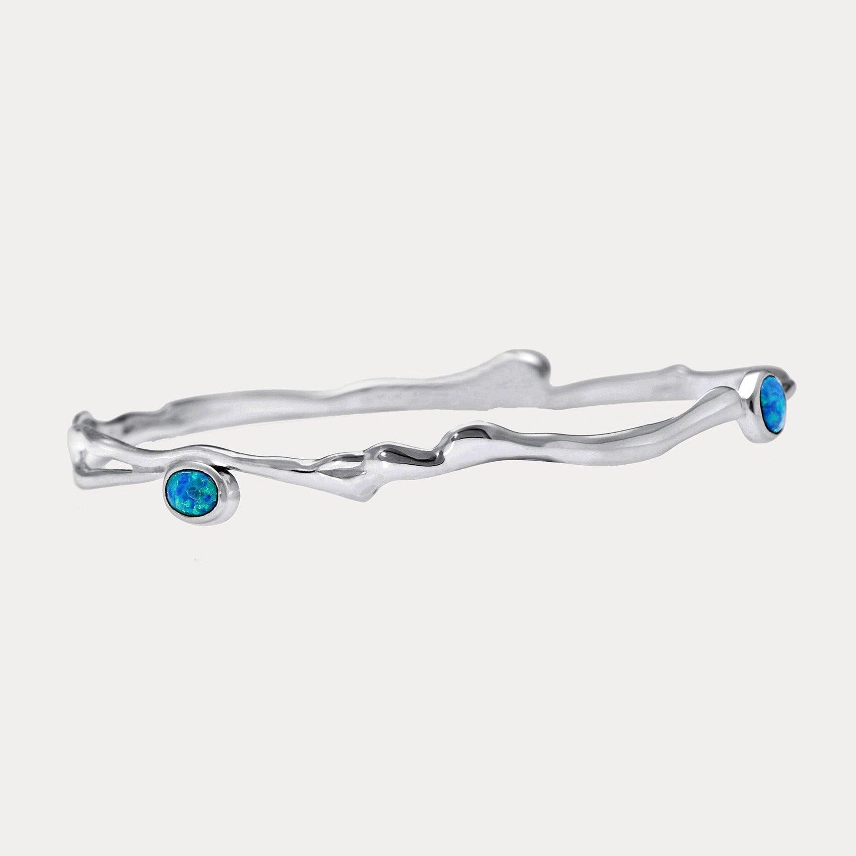 A Sterling Silver bangle bracelet with three Opal stones set in it, two blue and one white, against a white background.