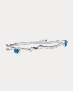 A Sterling Silver bangle bracelet with three Opal stones set in it, two blue and one white, against a white background.