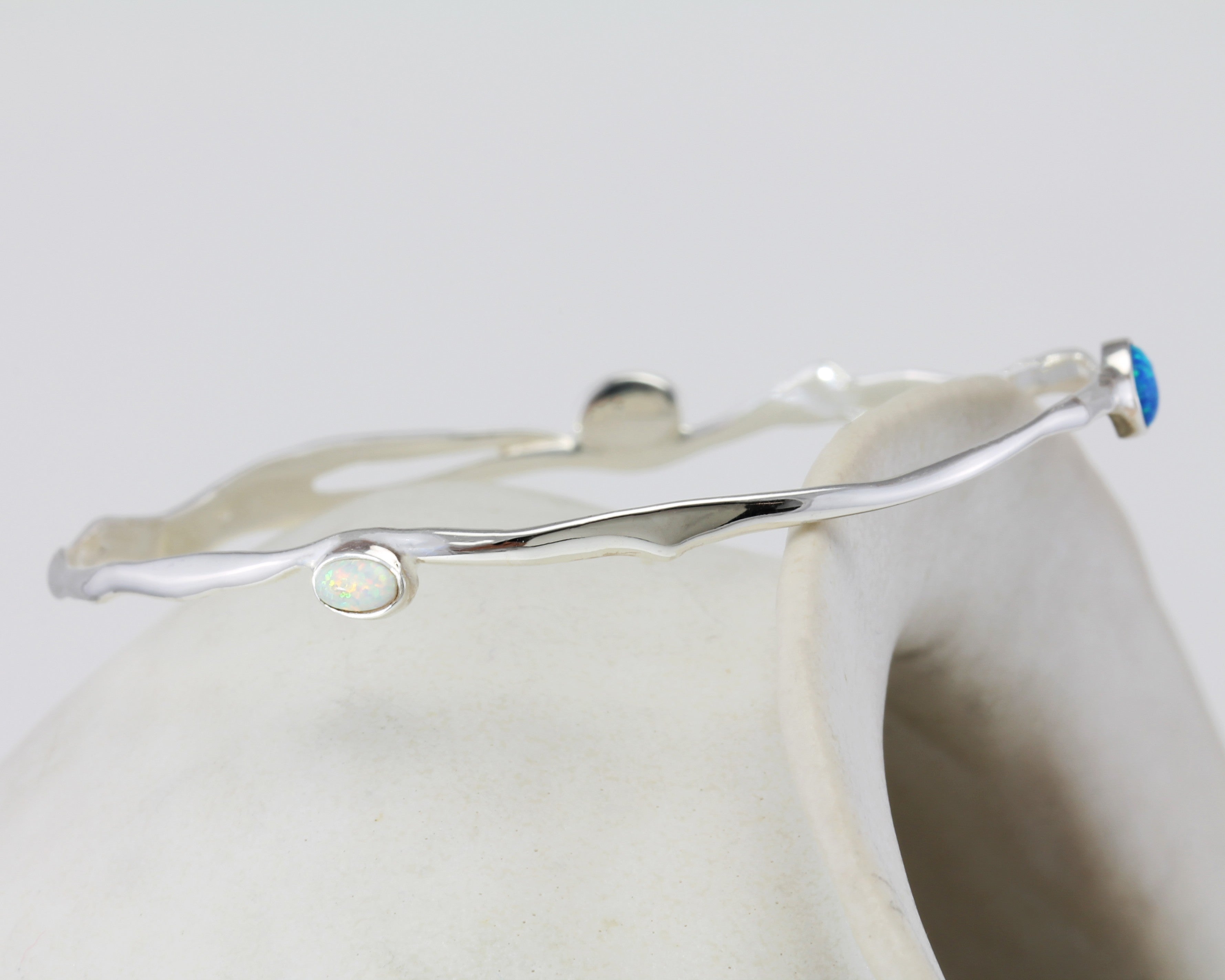 Silver bracelet with blue and white Opal gemstones on a white ceramic pot.