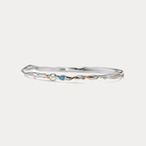 a slim silver bangle with opal and pearl stones and gold details