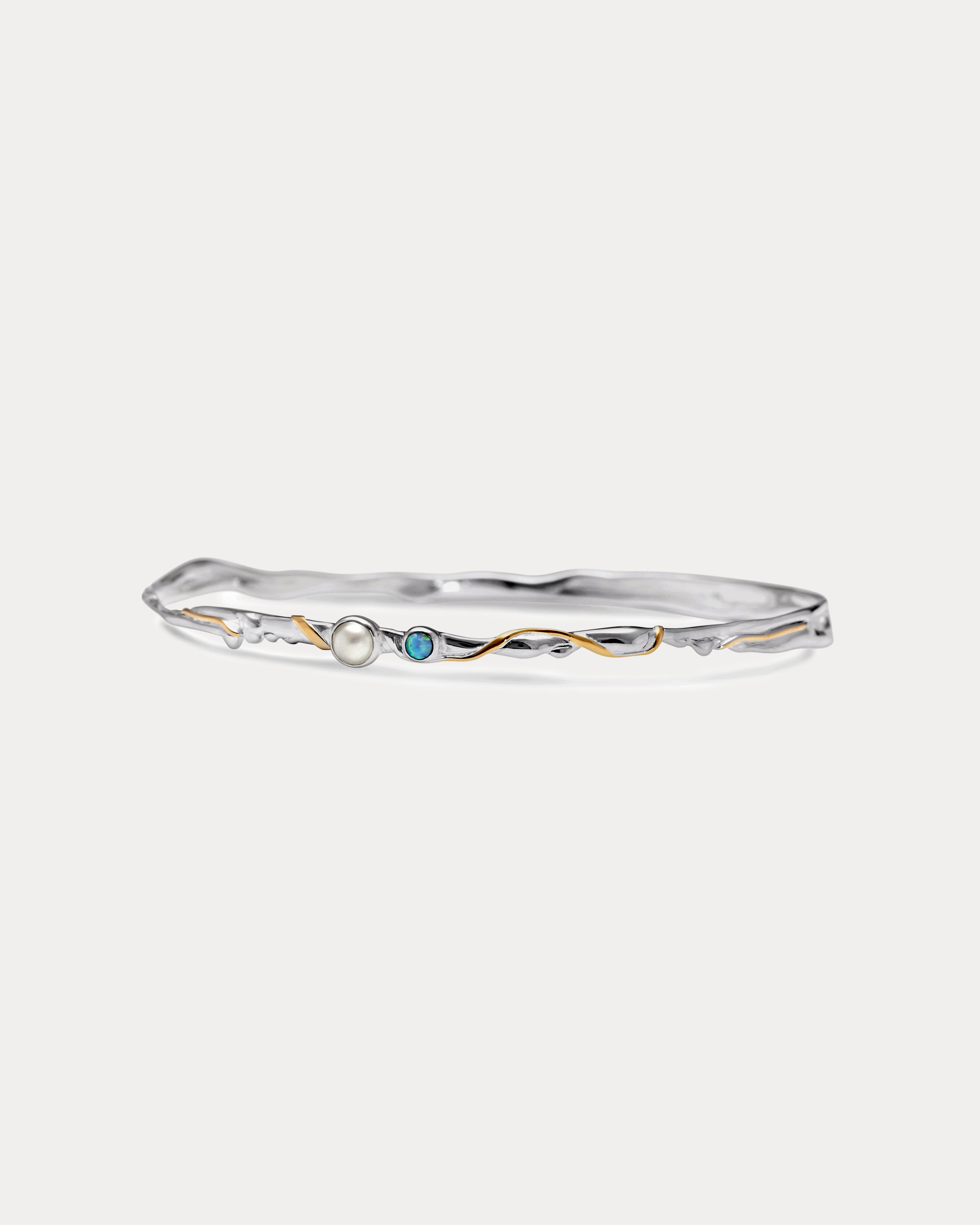 a slim silver bangle with opal and pearl stones and gold details