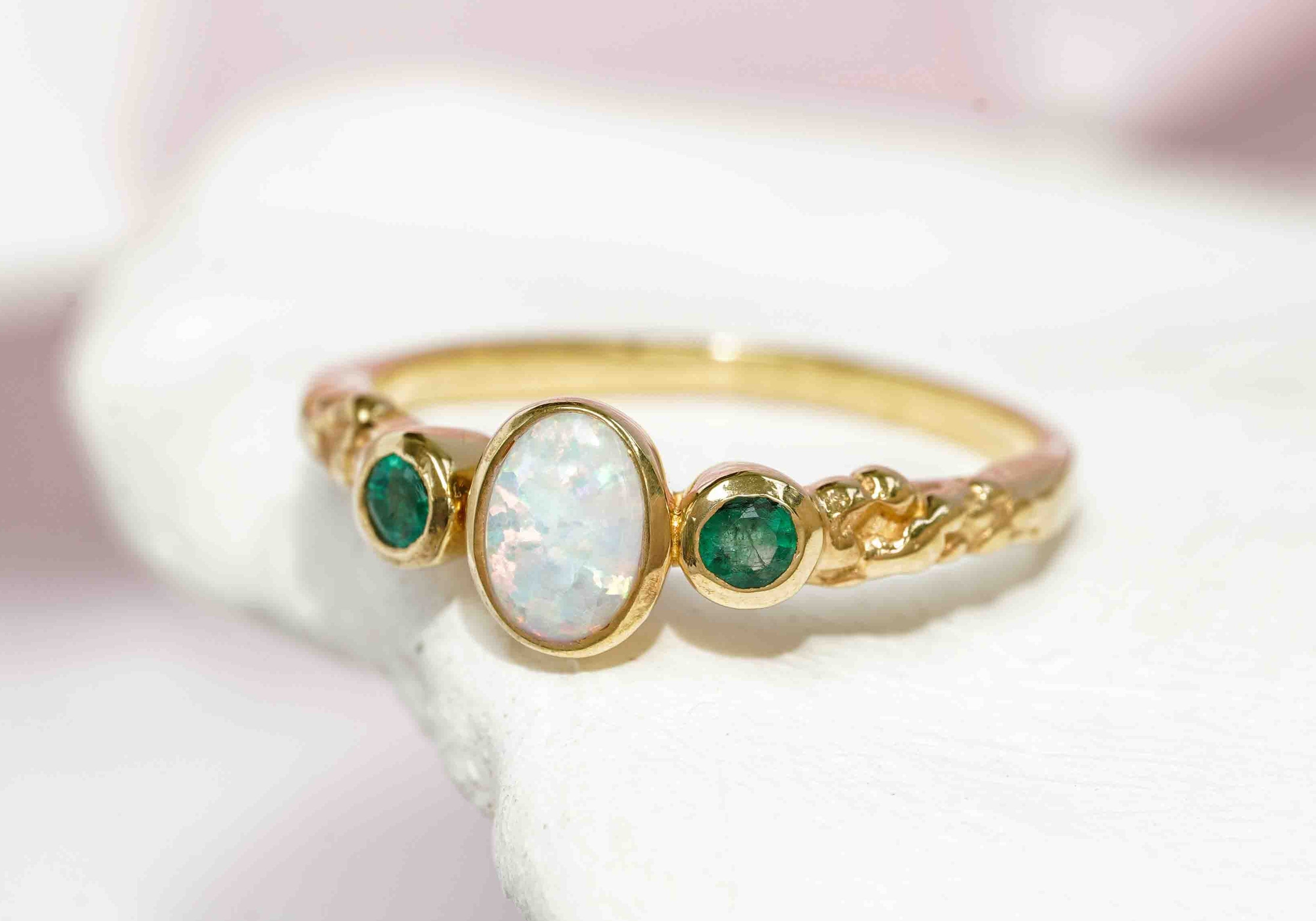 Textured gold ring set with two tiny green emeralds and oval white opalite.
