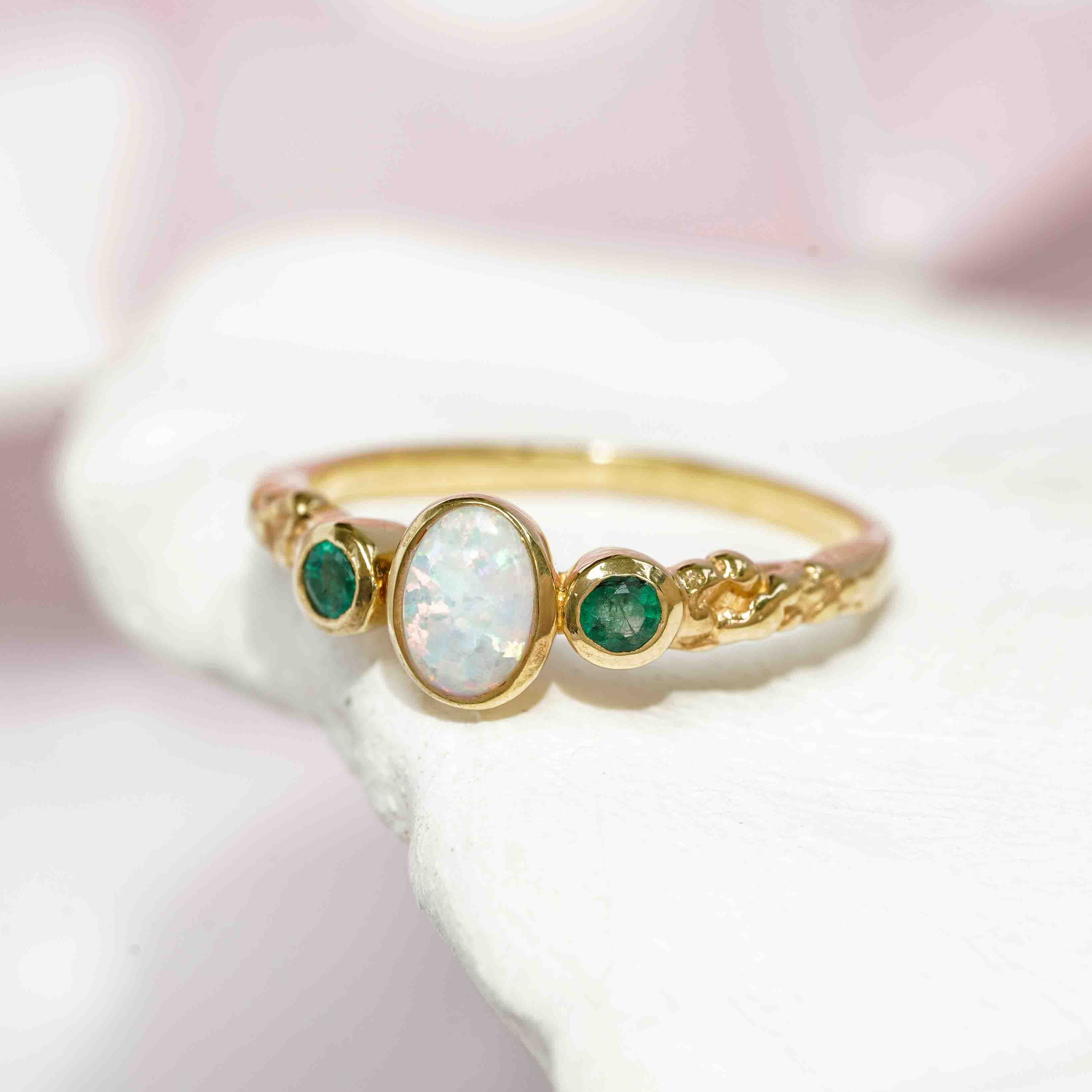 Textured gold ring set with two tiny green emeralds and oval white opalite.