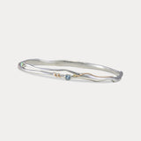 A Sterling Silver bangle bracelet with a small round blue Topaz and white Opal accented by 14KT Gold Fill Wire.