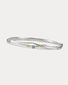 A Sterling Silver bangle bracelet with a small round blue Topaz and white Opal accented by 14KT Gold Fill Wire.