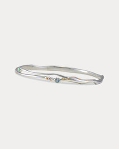A Sterling Silver bangle bracelet with a small round blue Topaz and white Opal accented by 14KT Gold Fill Wire.