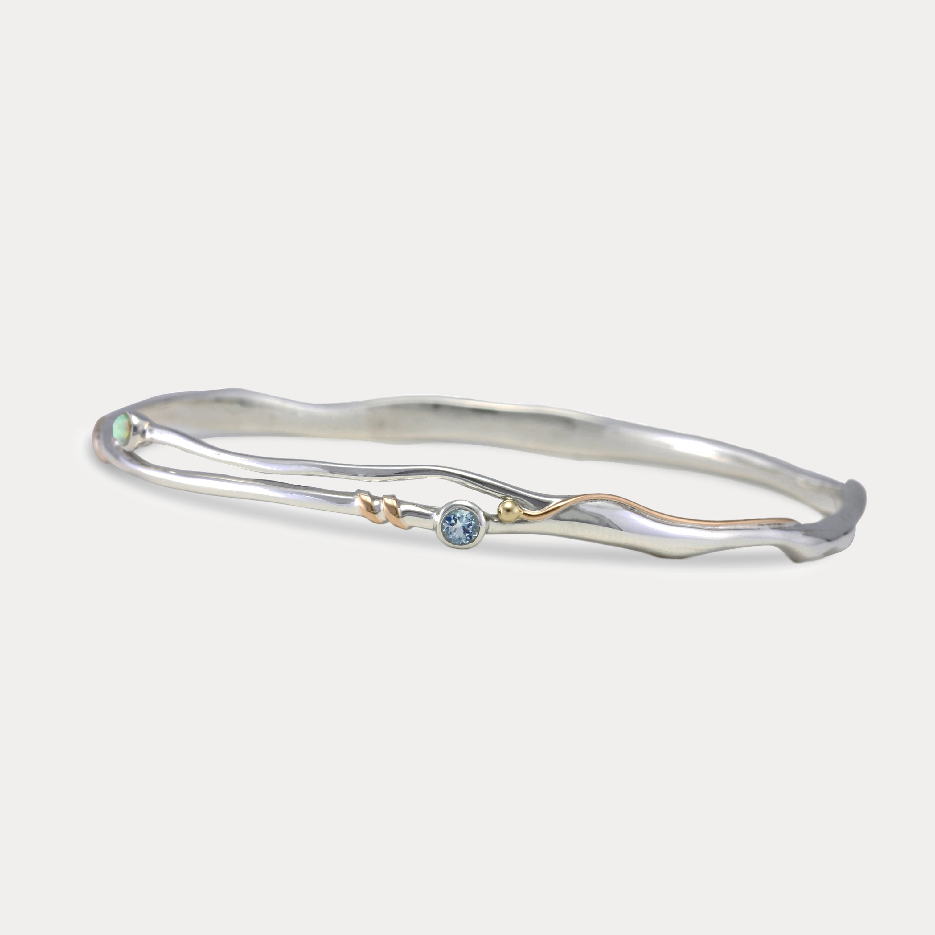 A Sterling Silver bangle bracelet with a small round blue Topaz and white Opal accented by 14KT Gold Fill Wire.