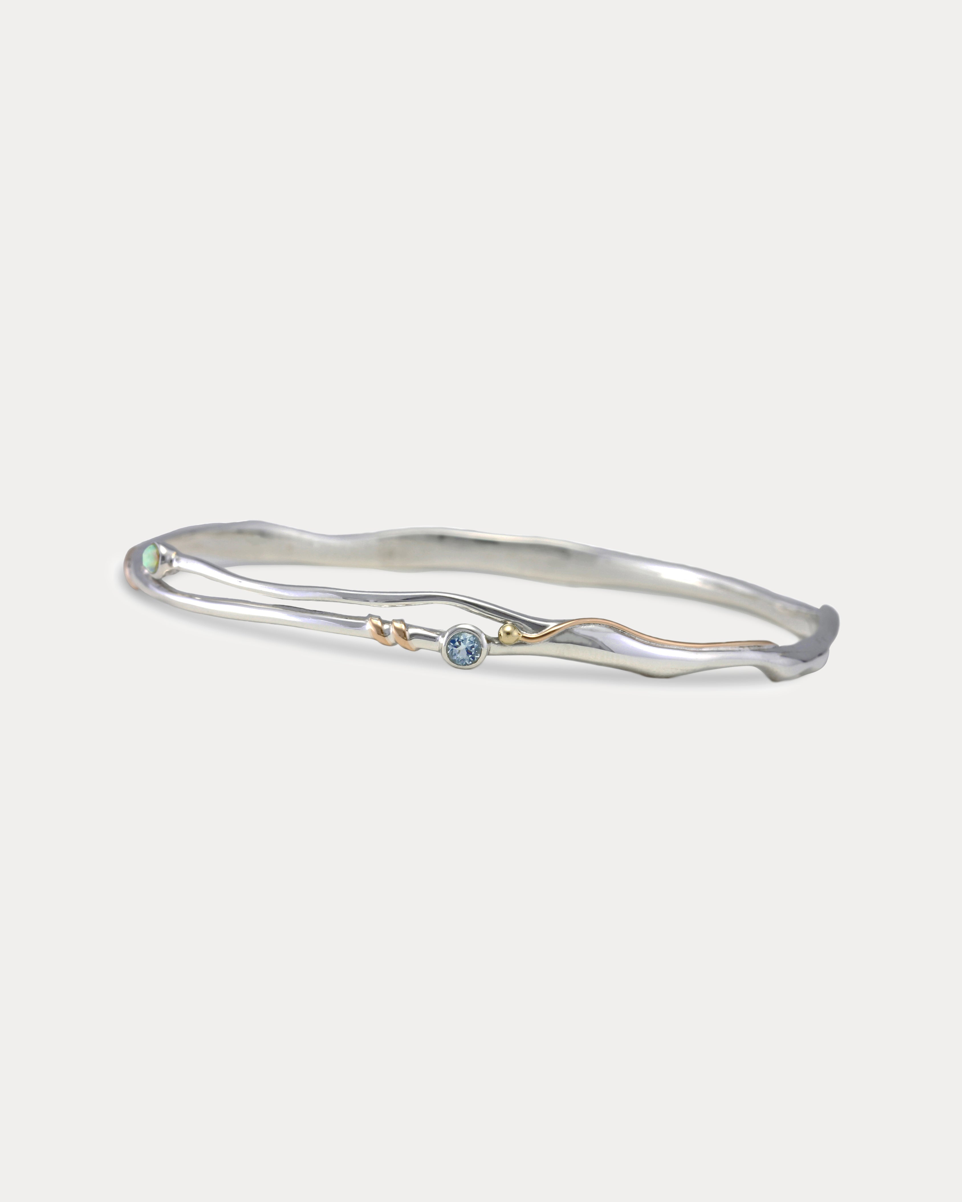 A Sterling Silver bangle bracelet with a small round blue Topaz and white Opal accented by 14KT Gold Fill Wire.