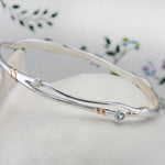 Silver bracelet with blue topaz and white opal on a floral-patterned fabric background