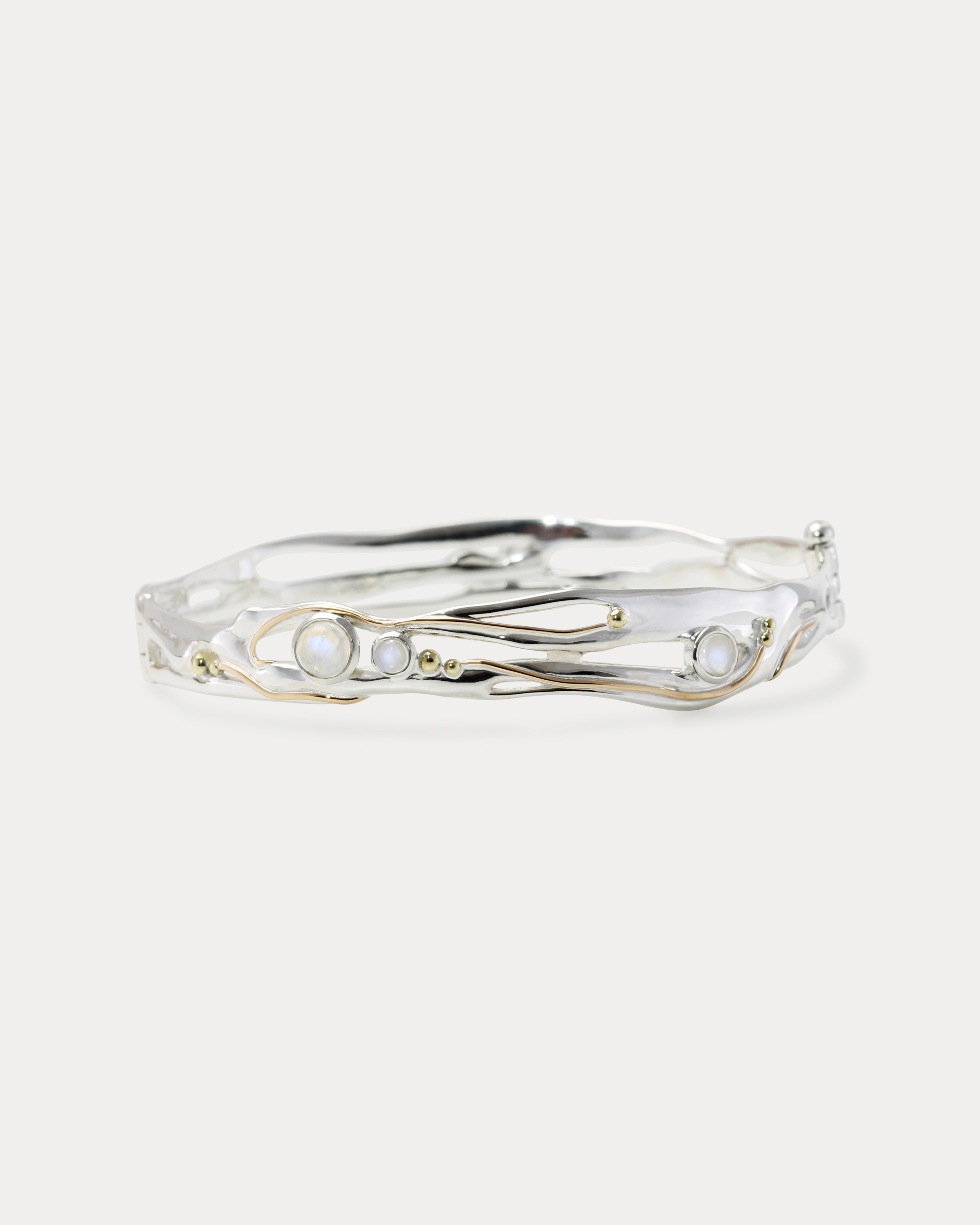 A handmade sterling silver bangle bracelet with moonstone and 14KT gold details, displayed against a white background.