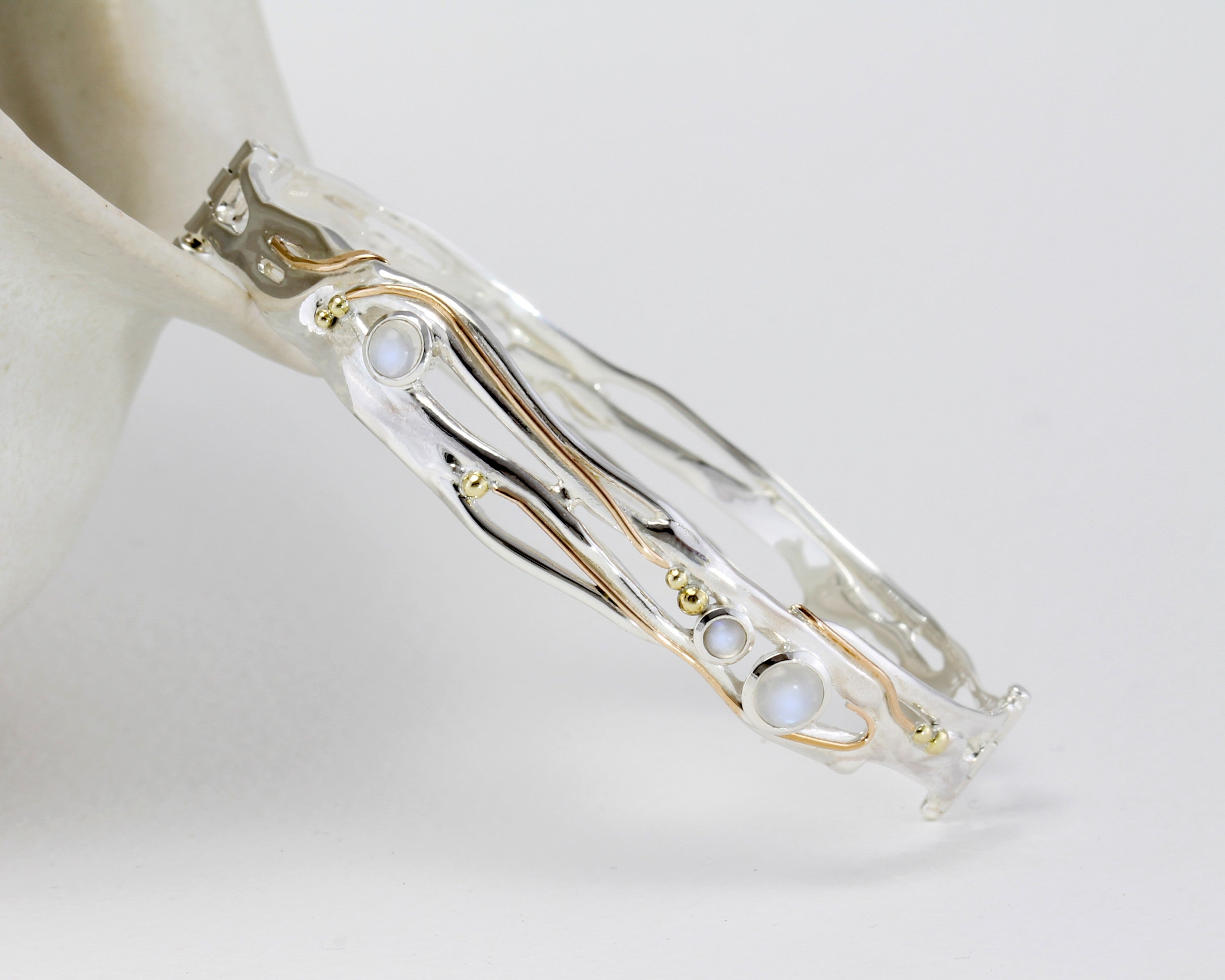 sterling silver bangle leant against ceramic pot with gold detailing and moonstones