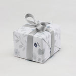 A ring box is beautifully wrapped in neutral tone floral gift wrapping finished with a silver ribbon.