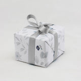 A ring box is beautifully wrapped in neutral tone floral gift wrapping finished with a silver ribbon.