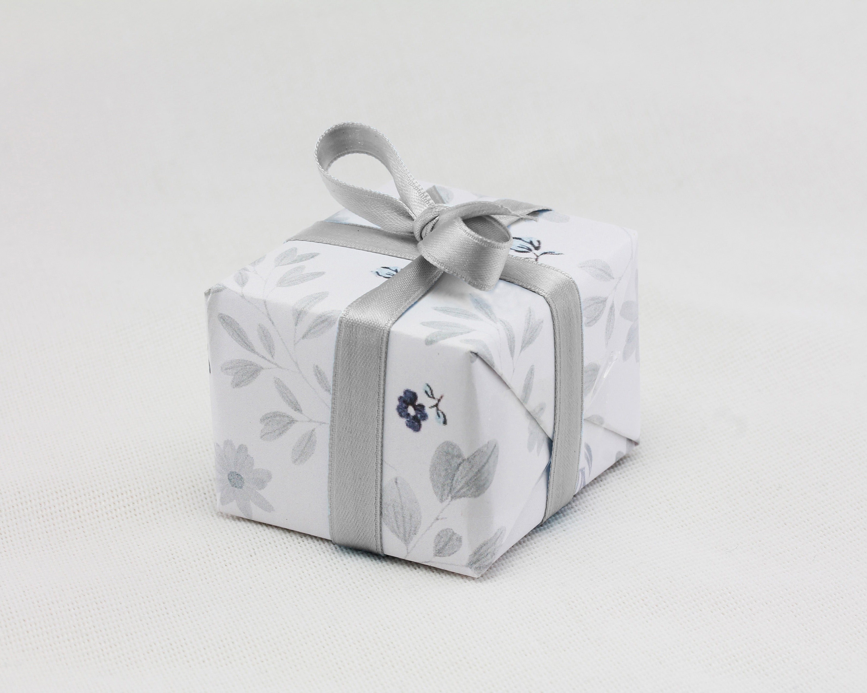 A ring box is beautifully wrapped in neutral tone floral gift wrapping finished with a silver ribbon.