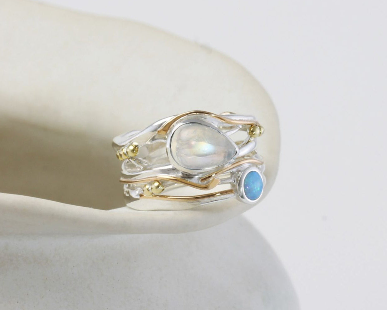 Silver and Gold ring with moonstone and blue gemstone on a white surface