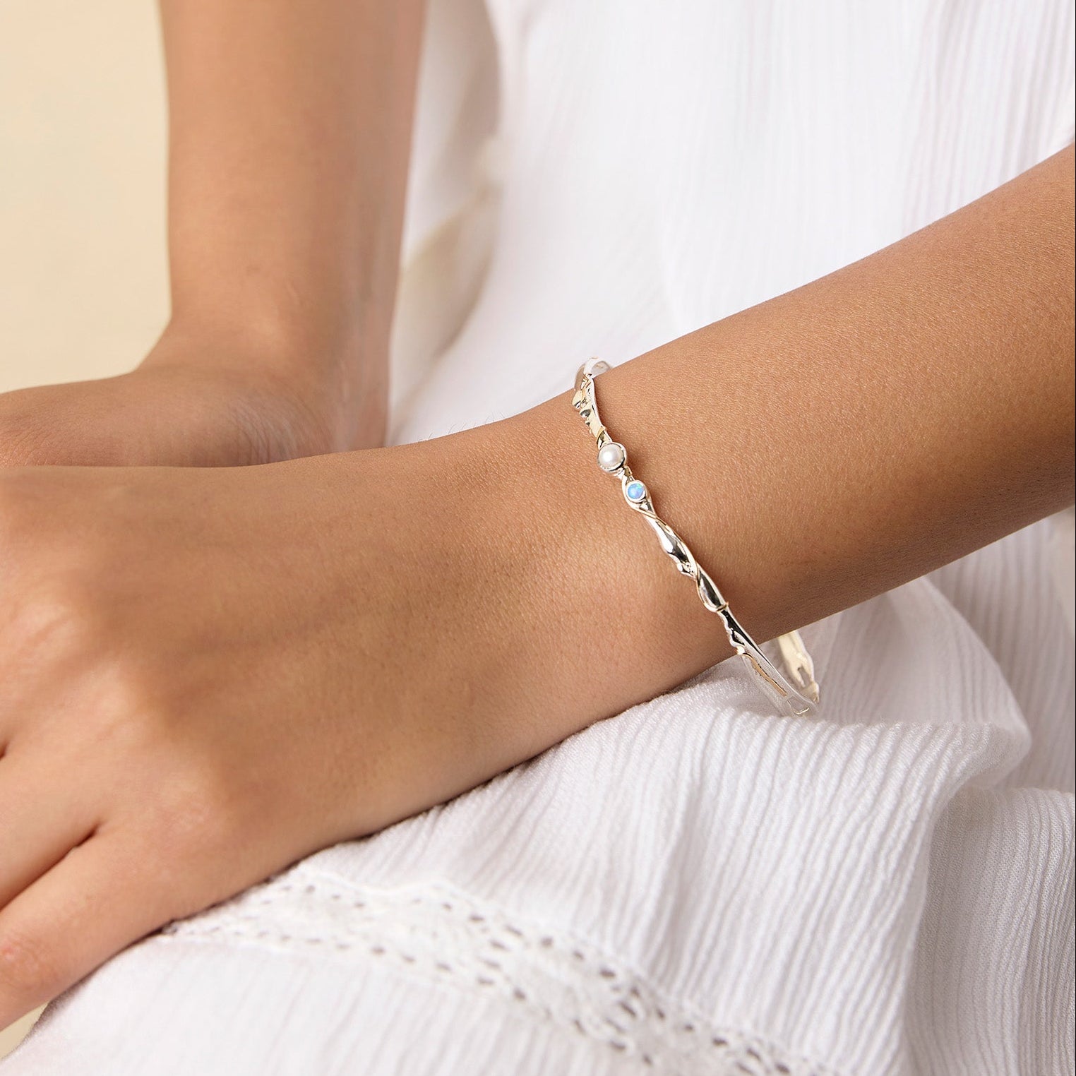 model wearing a delicate sterling silver bangle with blue and white gemstones