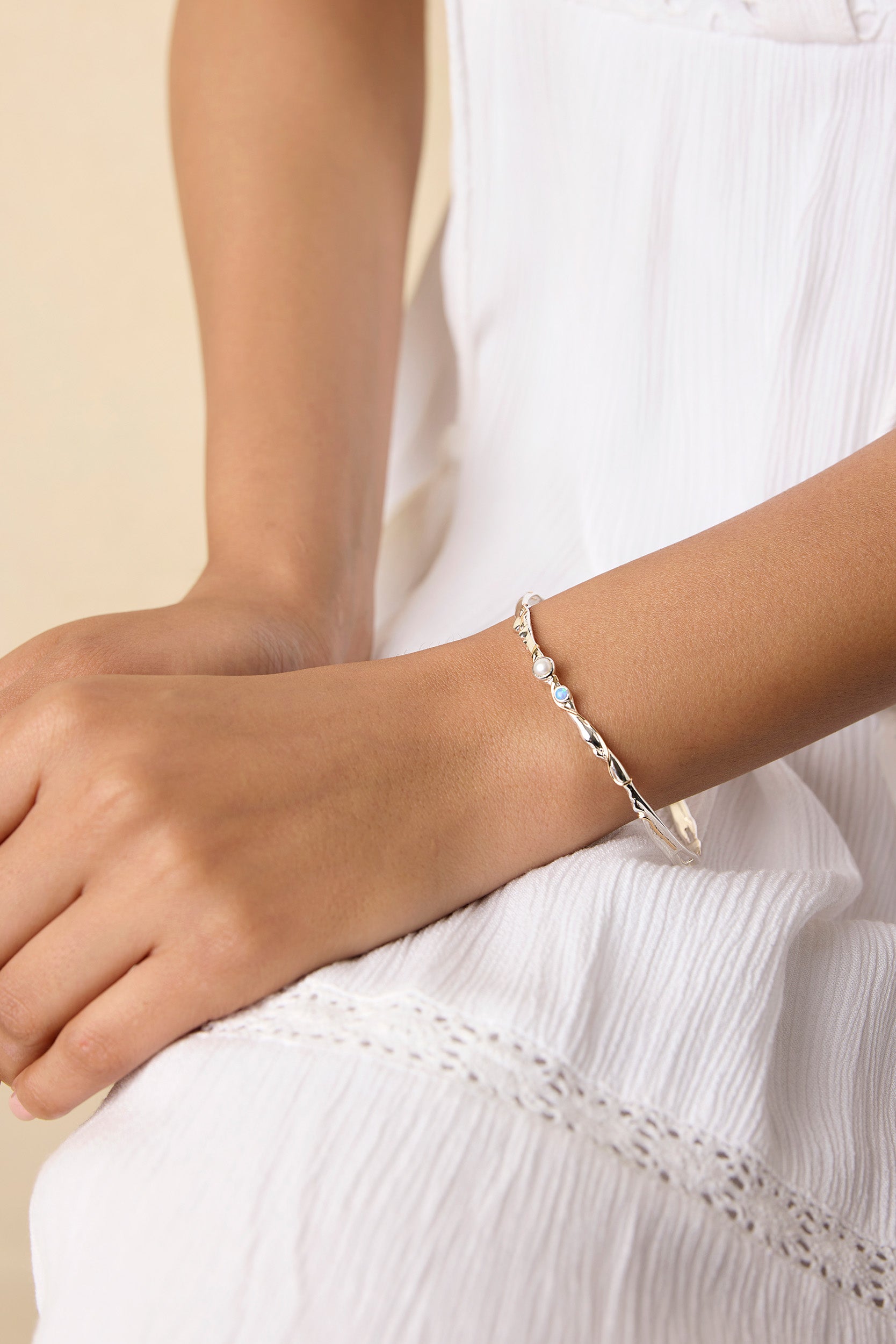 model wearing a delicate sterling silver bangle with blue and white gemstones