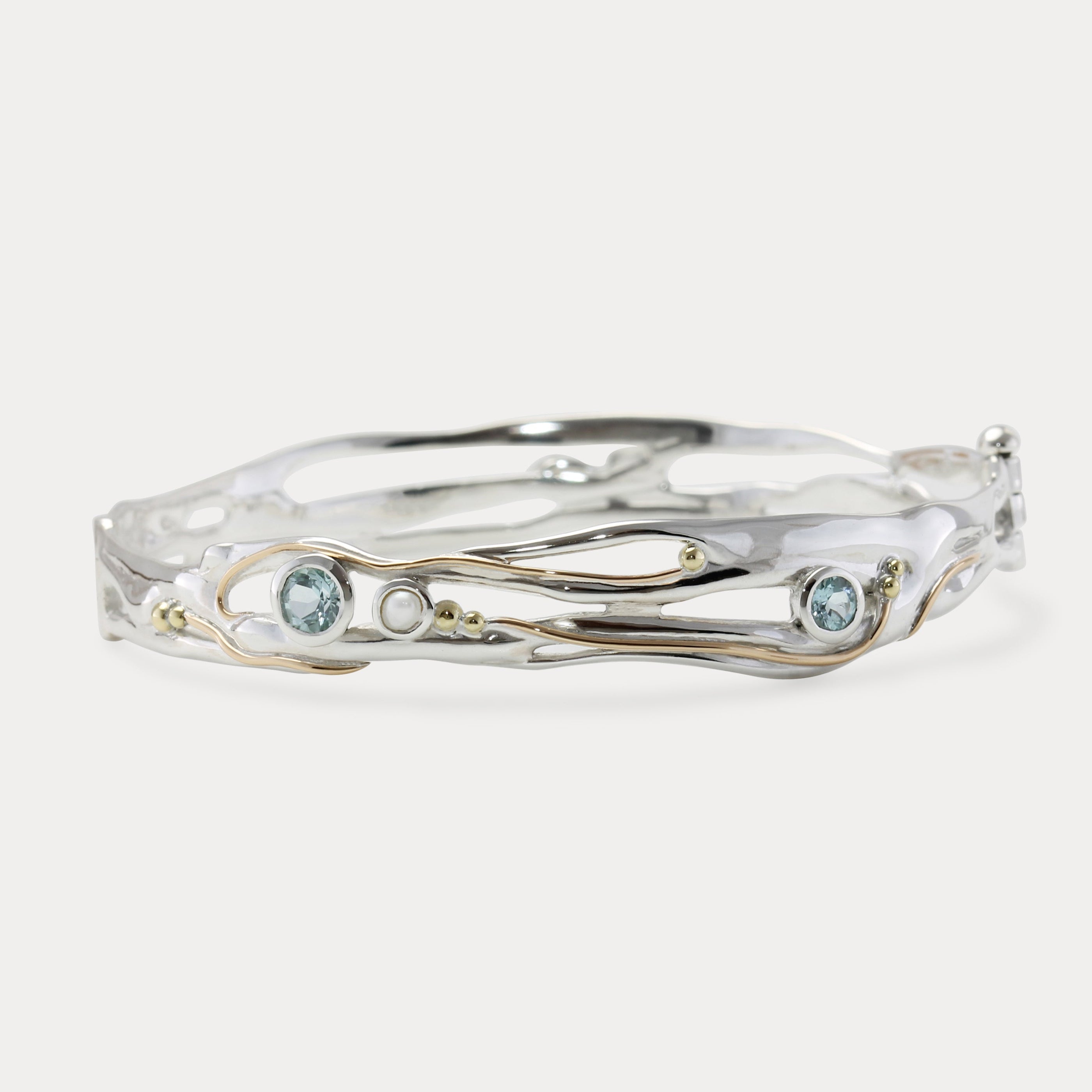 A Sterling Silver bangle featuring round Blue Topaz and a Freshwater Pearl, with 14KT Gold detailing.
