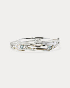 A Sterling Silver bangle featuring round Blue Topaz and a Freshwater Pearl, with 14KT Gold detailing.