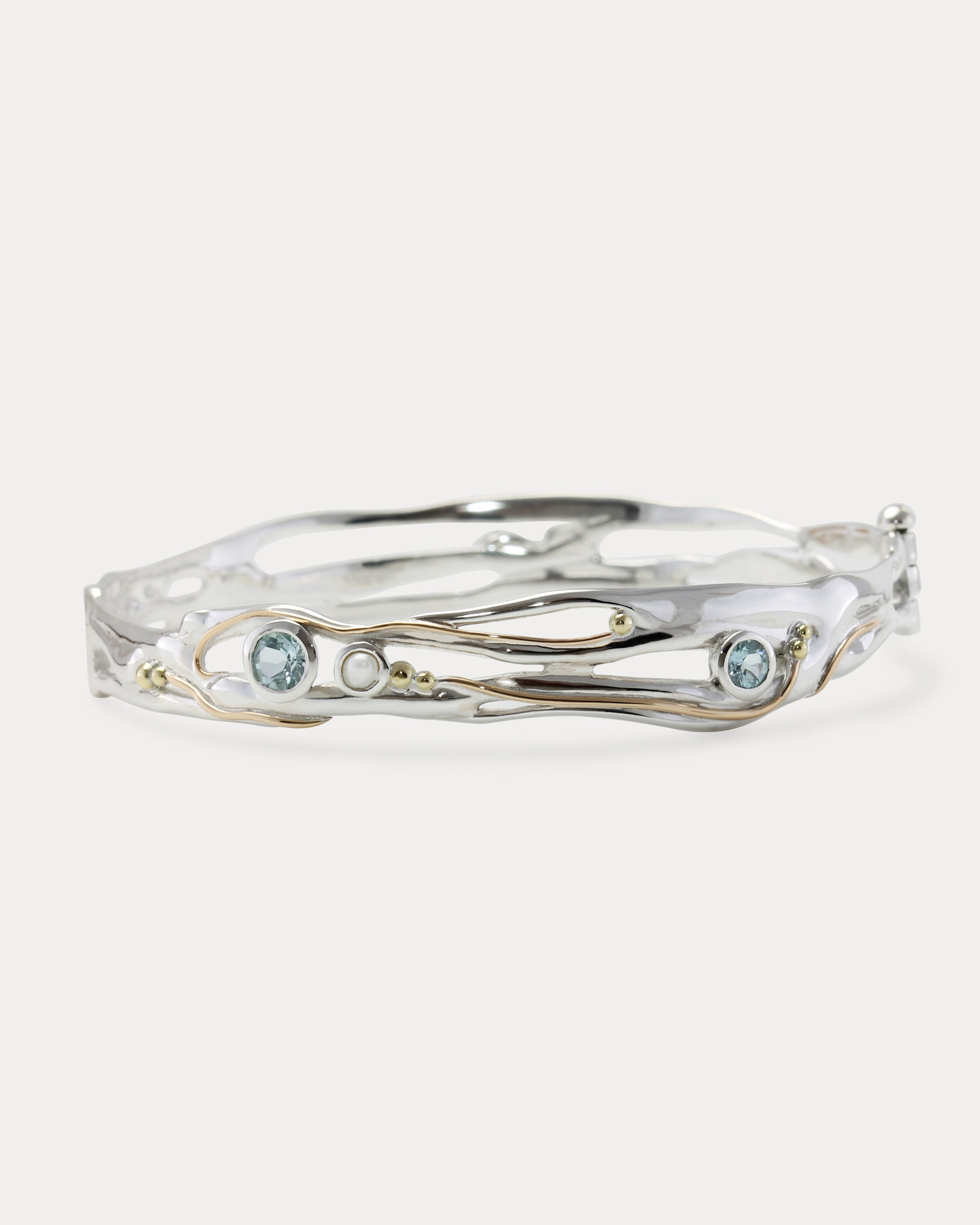 A Sterling Silver bangle featuring round Blue Topaz and a Freshwater Pearl, with 14KT Gold detailing.