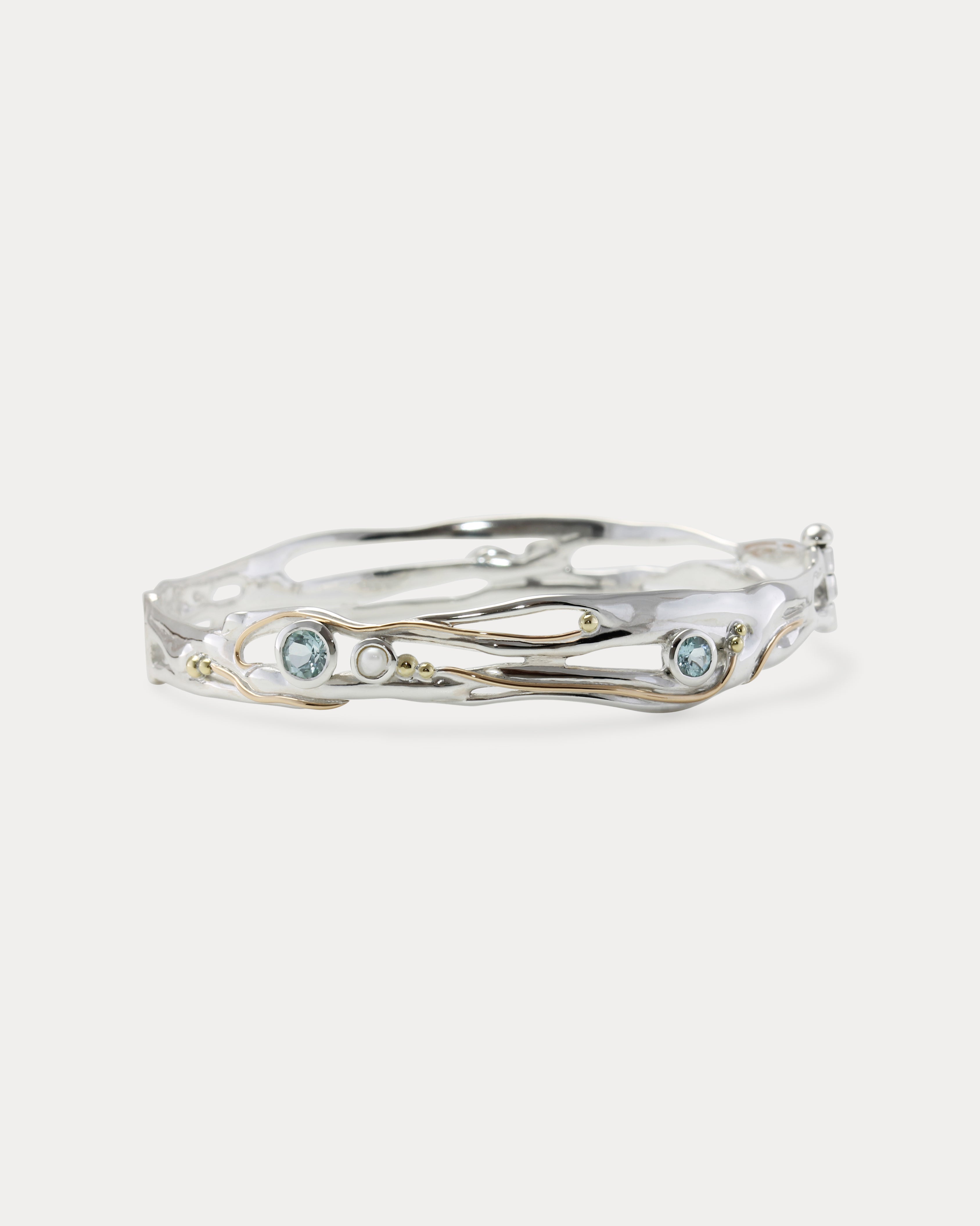 A Sterling Silver bangle featuring round Blue Topaz and a Freshwater Pearl, with 14KT Gold detailing.