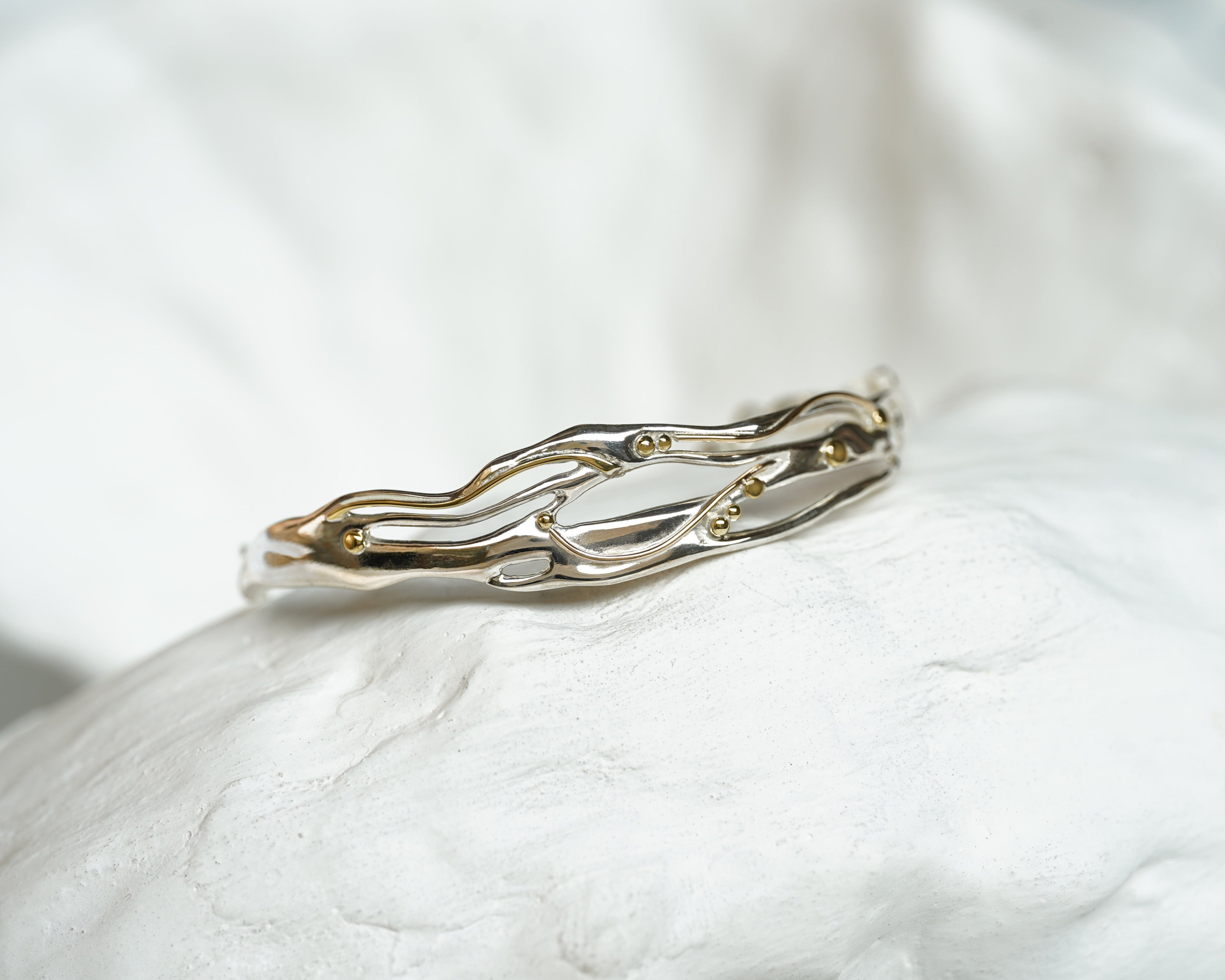 silver and gold statement bracelet on a textured stone