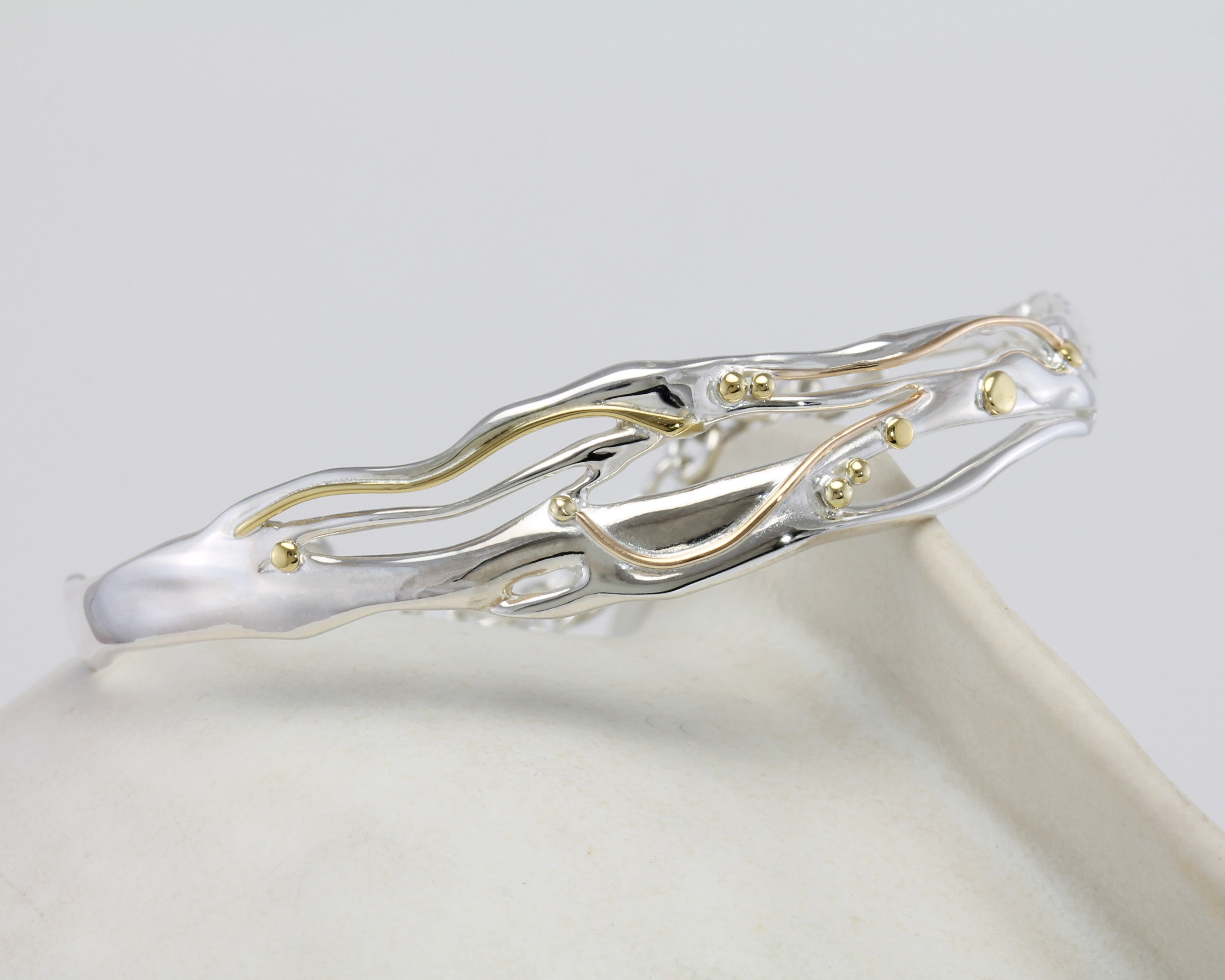 flowing silver and gold bracelet on a ceramic pot