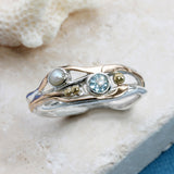 Gold and silver ring with gemstones on a textured surface with flowers.