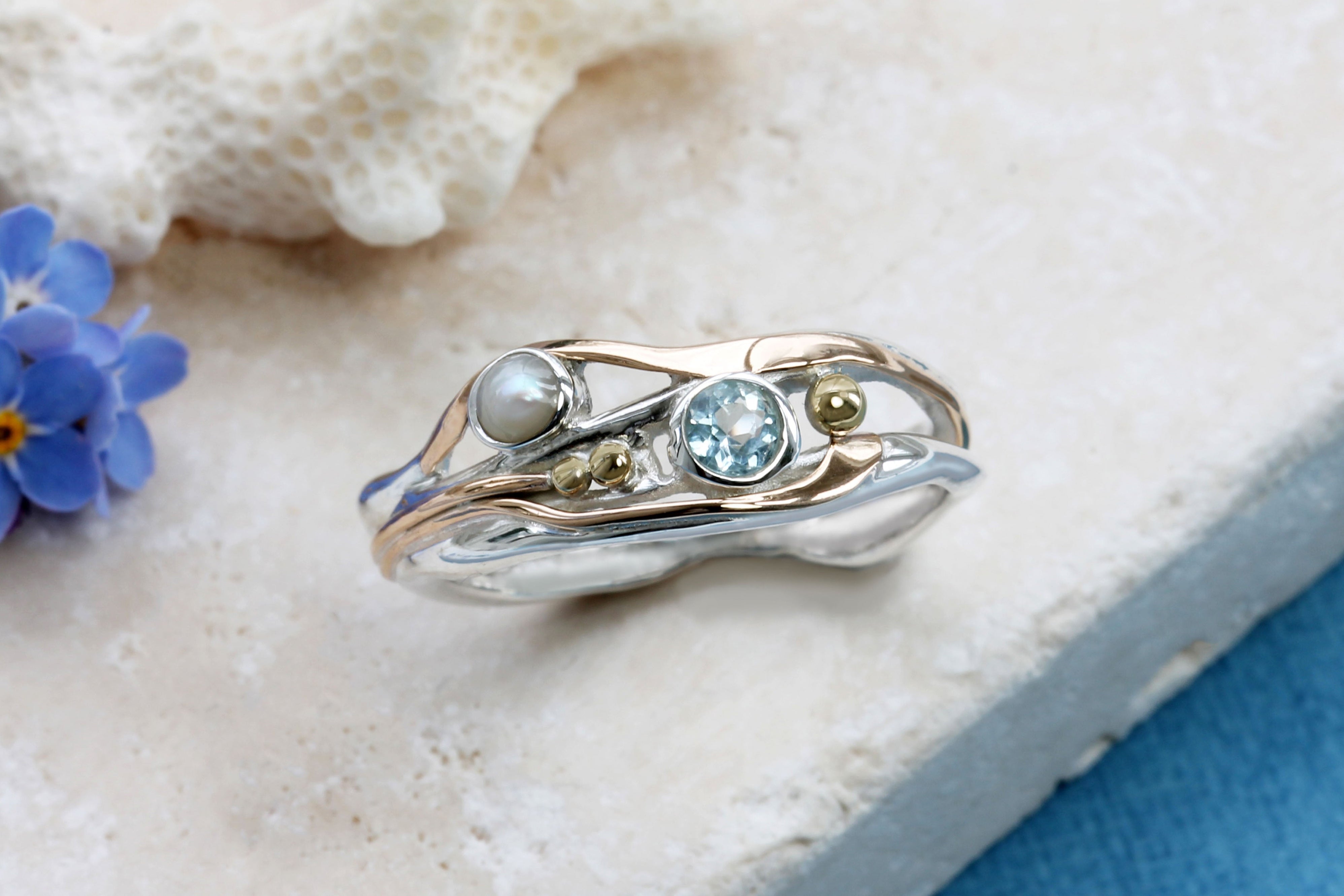 Gold and silver ring with gemstones on a textured surface with flowers.