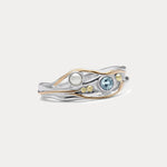 A Sterling Silver ring with a faceted Blue Topaz and a Freshwater Pearl, accented with 14kt gold detailing, displayed against a white background.