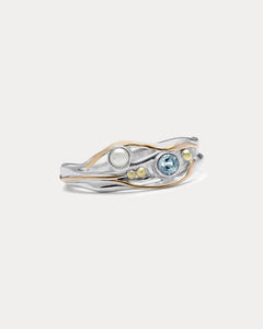 A Sterling Silver ring with a faceted Blue Topaz and a Freshwater Pearl, accented with 14kt gold detailing, displayed against a white background.