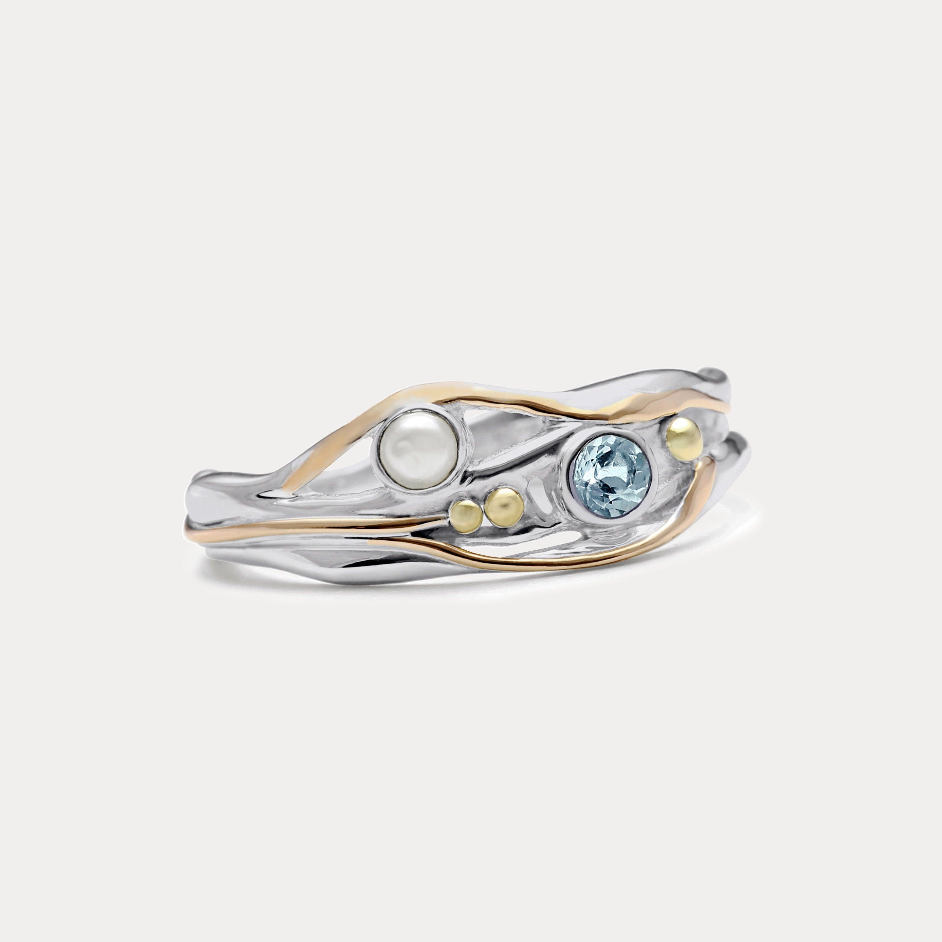 A Sterling Silver ring with a faceted Blue Topaz and a Freshwater Pearl, accented with 14kt gold detailing, displayed against a white background.