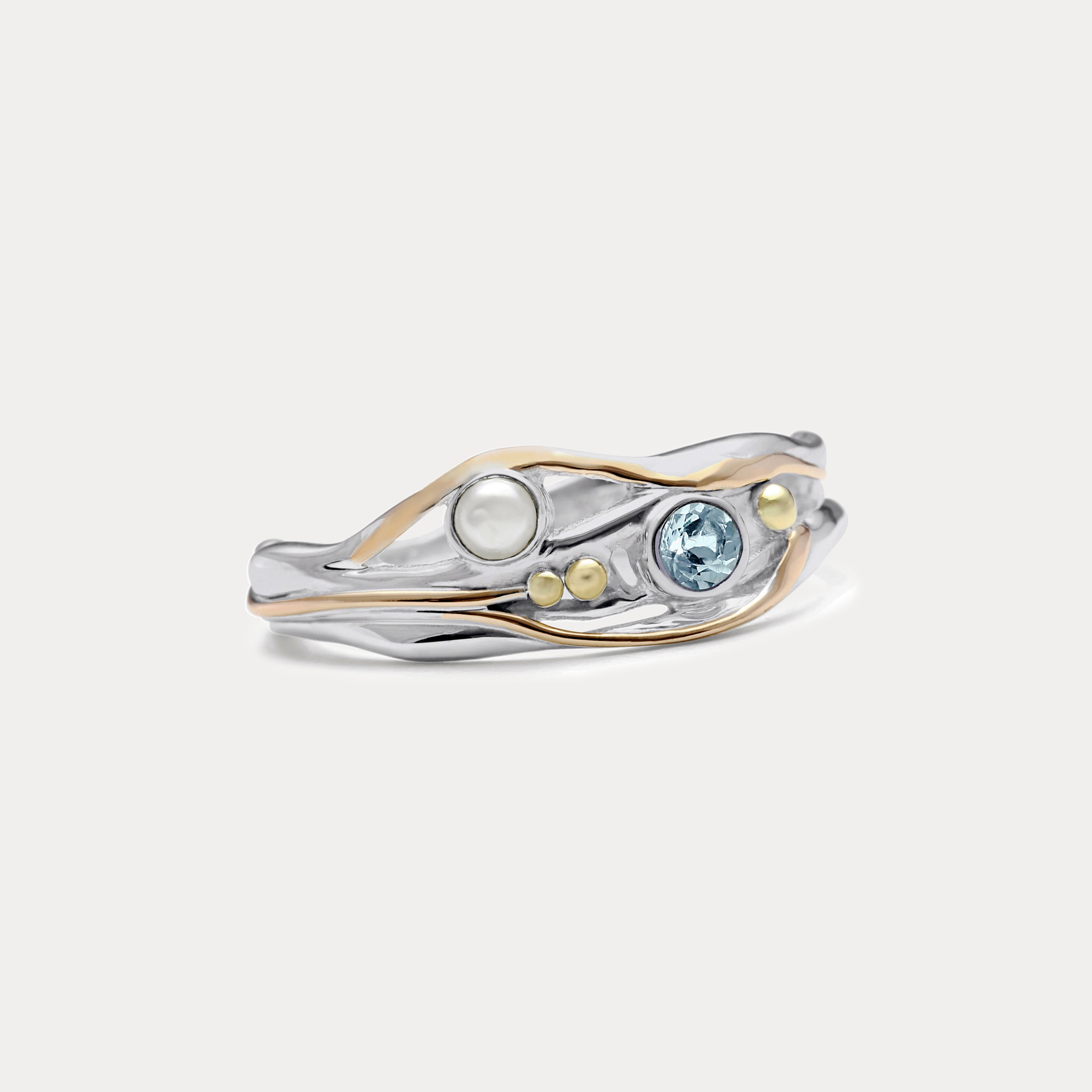 A Sterling Silver ring with a faceted Blue Topaz and a Freshwater Pearl, accented with 14kt gold detailing, displayed against a white background.