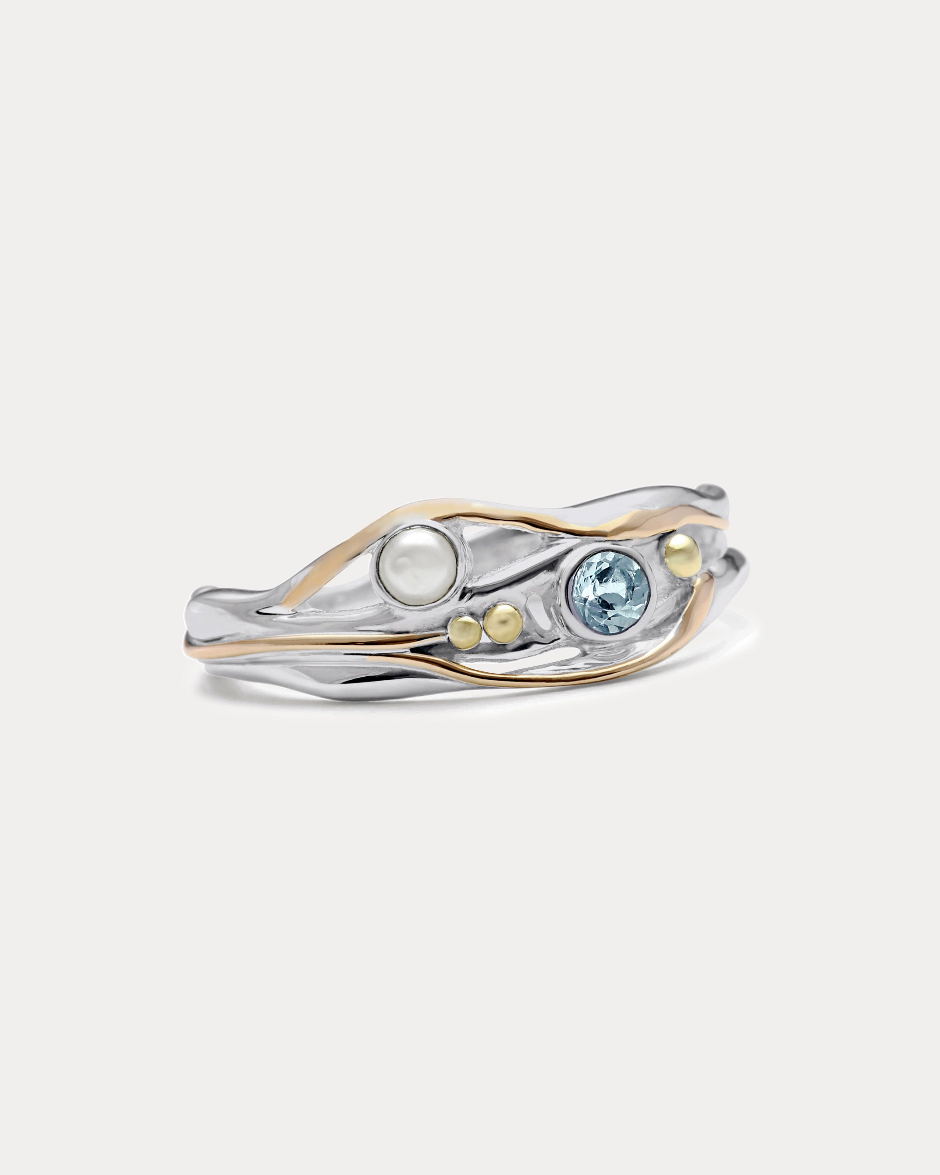 A Sterling Silver ring with a faceted Blue Topaz and a Freshwater Pearl, accented with 14kt gold detailing, displayed against a white background.