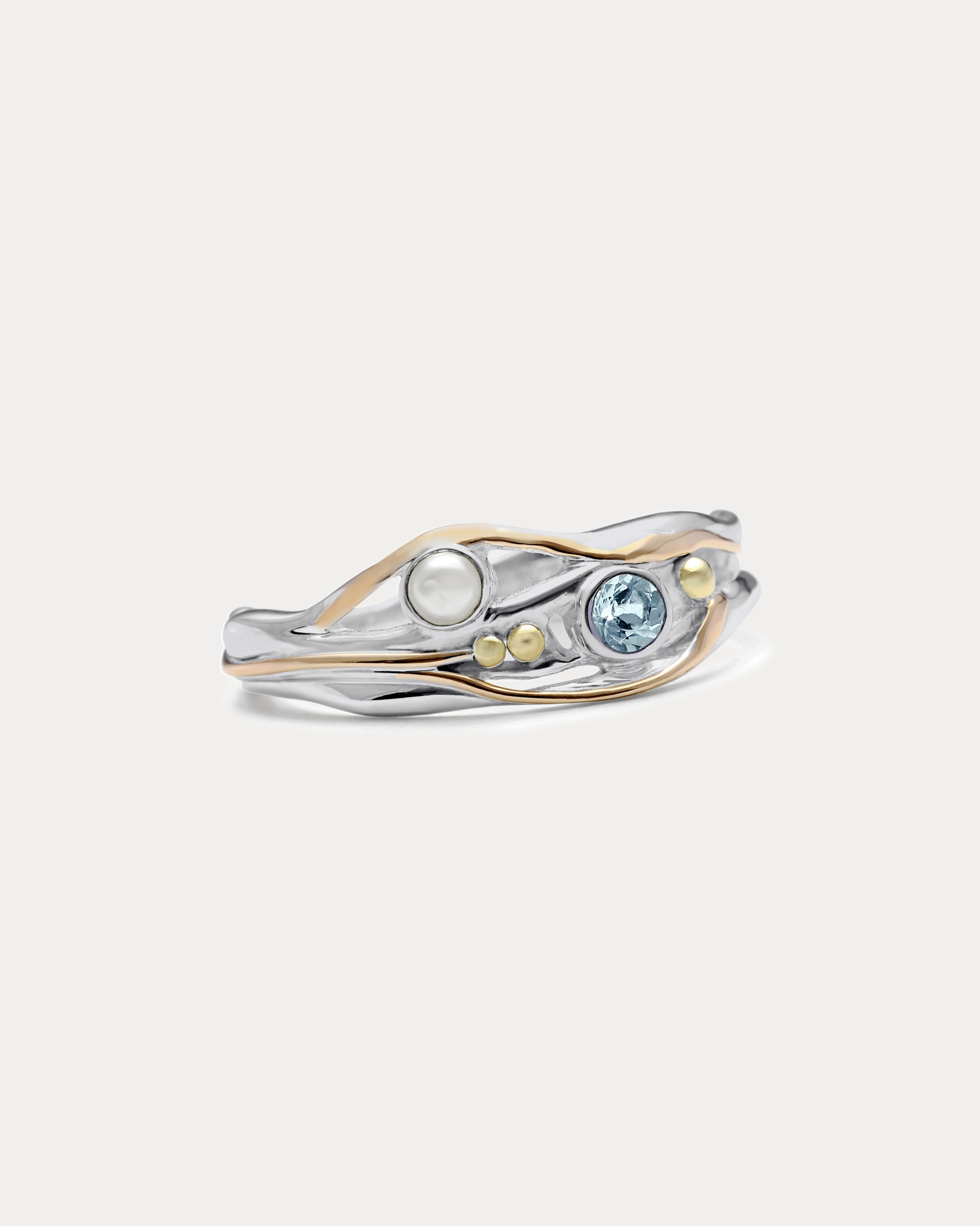 A Sterling Silver ring with a faceted Blue Topaz and a Freshwater Pearl, accented with 14kt gold detailing, displayed against a white background.