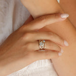 Close-up of a hand wearing a silver and gold ring with a gemstone on a neutral background