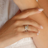 Close-up of a hand wearing a silver and gold ring with a gemstone on a neutral background