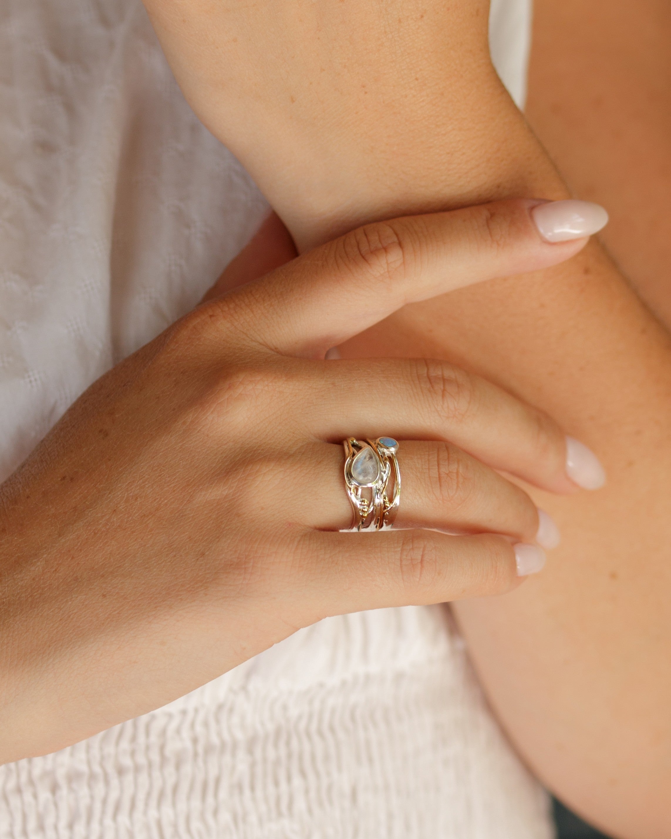 Close-up of a hand wearing a silver and gold ring with a gemstone on a neutral background
