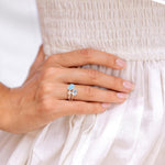 Close-up of a hand wearing a ring with a blue gemstone topaz and larimar and a white pearl against a white background