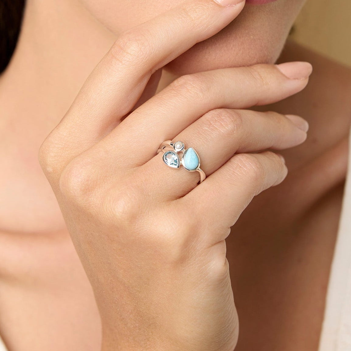 Woman wearing a ring with a blue gemstones, posing thoughtfully with hand on chin.