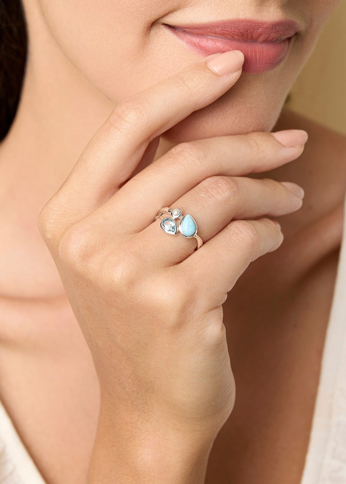 Woman wearing a ring with a blue gemstones, posing thoughtfully with hand on chin.