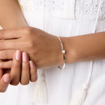 model wears a slim silver bangle with one white opal and two blue