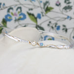 Silver bracelet with pearl and blue stone on a white pot with a floral background.