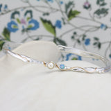 Silver bracelet with pearl and blue stone on a white pot with a floral background.